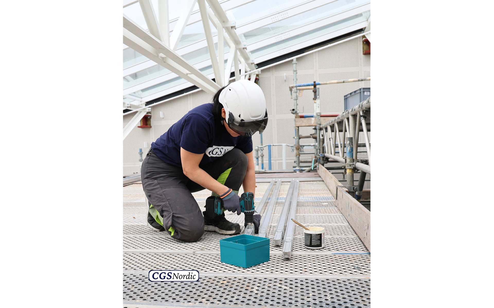 Rope access technician in safety harness suspended from H-RAIL system, working alongside the glazed wall of a building atrium for maintenance and inspection.