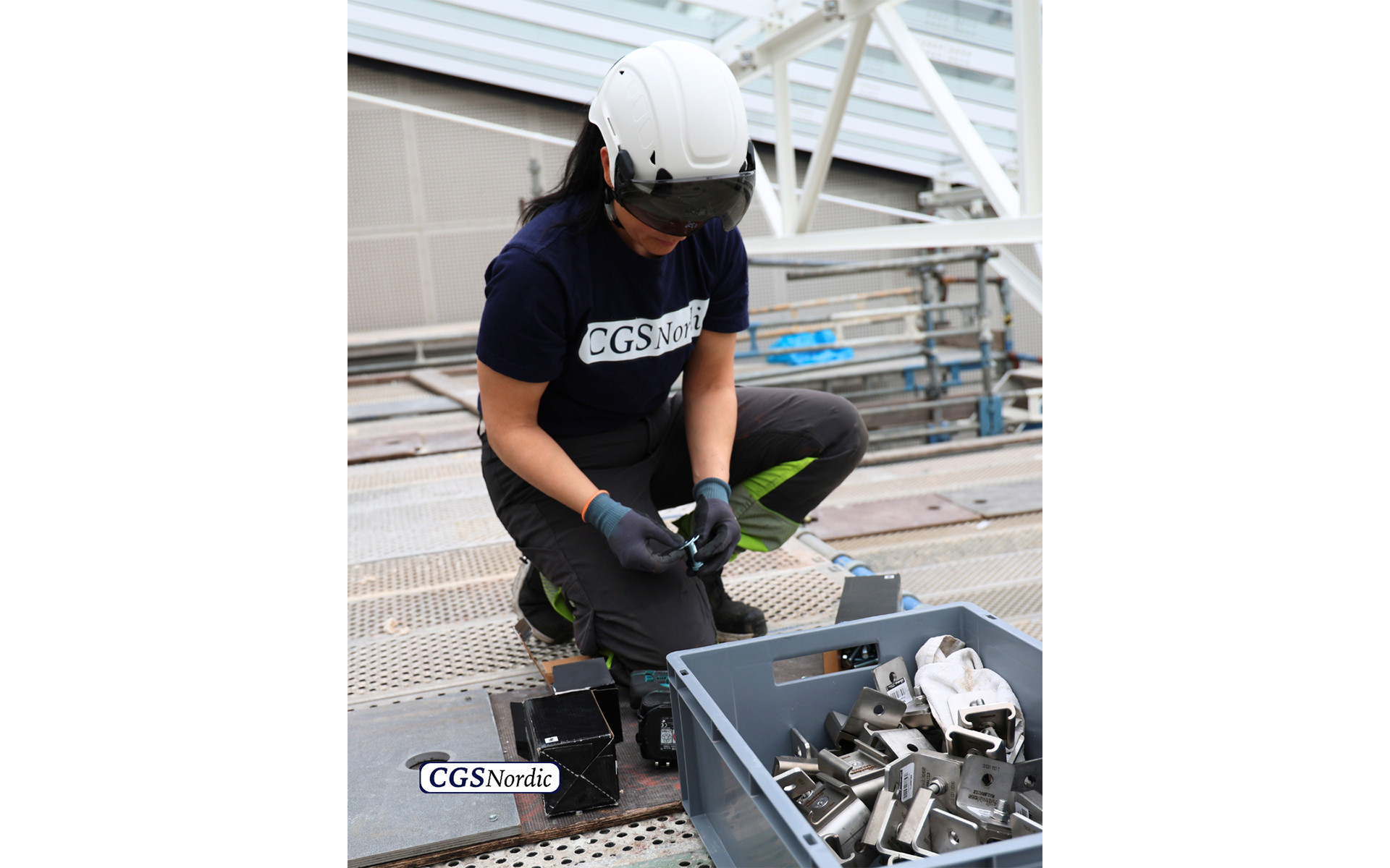 Full body view of a rope access technician in complete safety equipment suspended from H-RAIL system inside a glazed atrium, performing maintenance work at height.